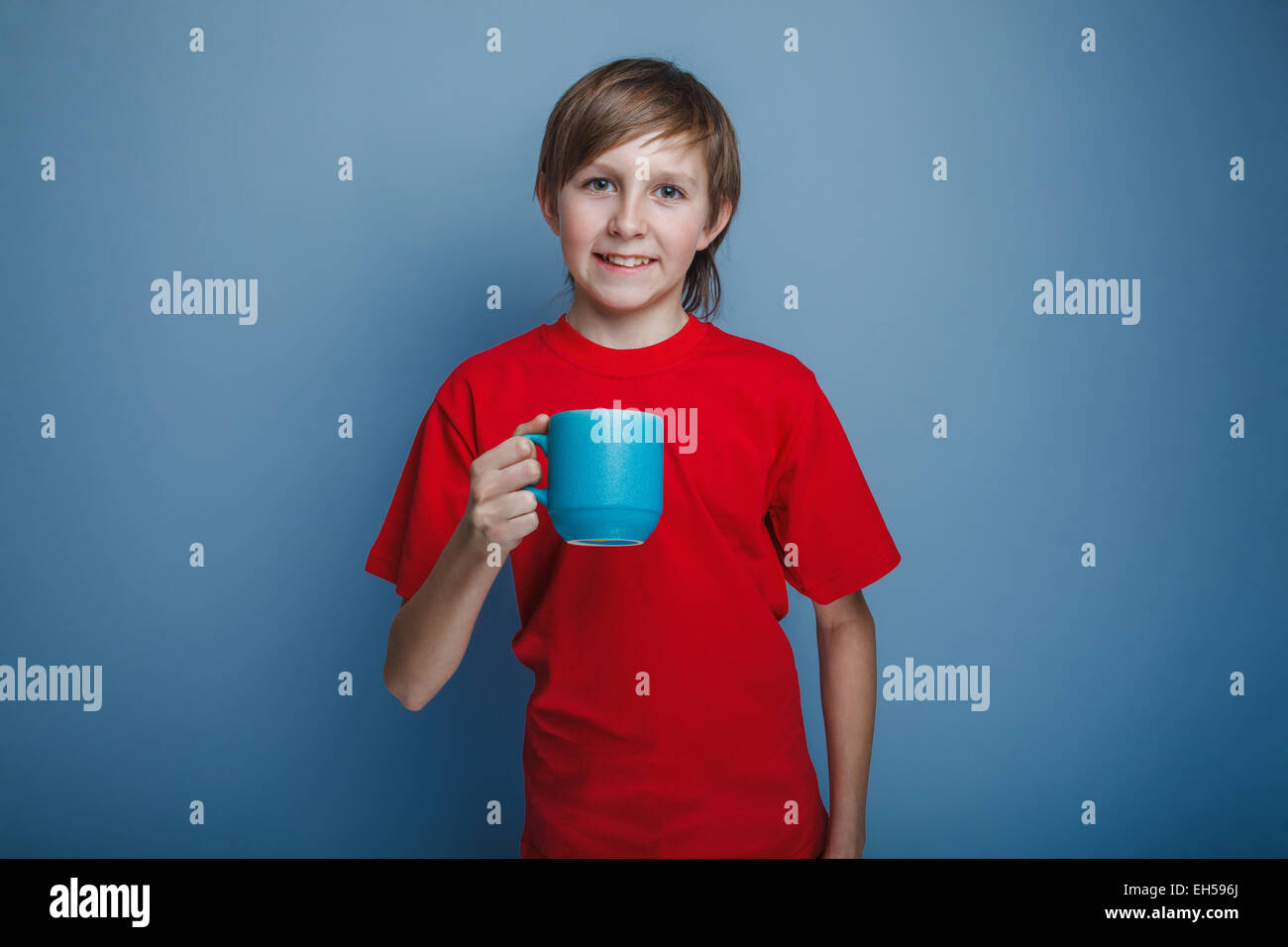 Europäisch - aussehenden jungen von zehn Jahren hält einen Becher auf einem grauen Hintergrund Stockfoto