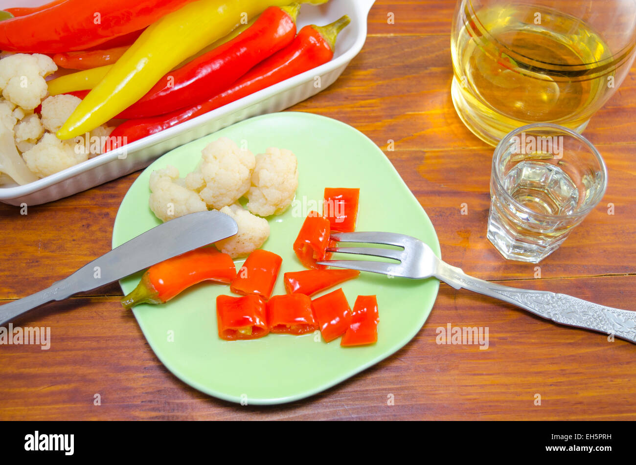 Eingelegte Paprika, Blumenkohl und Oliven auf einer Platte mit einem Messer und eine Gabel und einen Schuss Brandy Stockfoto