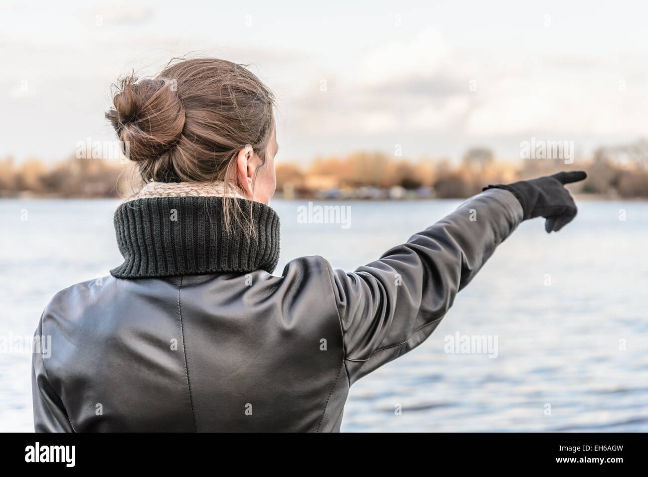 Ein Erwachsener mit einem Chignon und tragen ein schwarzes Leder Mantel Aufenthalte in der Nähe des Flusses und zeigen ihre Finger um etwas anzuzeigen Int Stockfoto