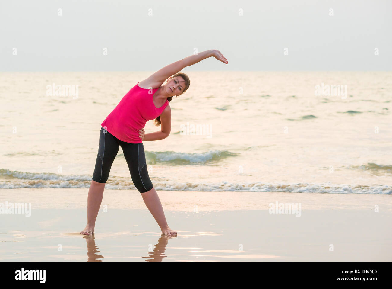 Frau in einem rosa Hemd Übungen auf dem nassen sand Stockfoto