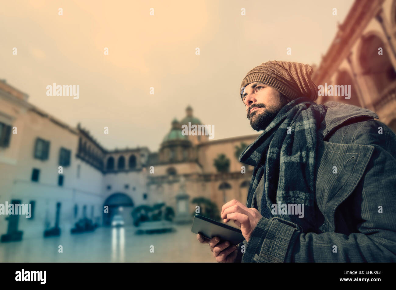 Junge Hipster lesen eine Tablette in einer unprätentiösen Platz mit einer Kirche auf dem Hintergrund in Instagram getönten Stil Stockfoto