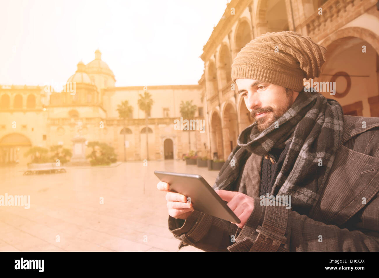 Junge Mann liest eine Tablette in einer unprätentiösen Platz mit einer Kirche auf dem Hintergrund in Instagram getönten Stil Stockfoto