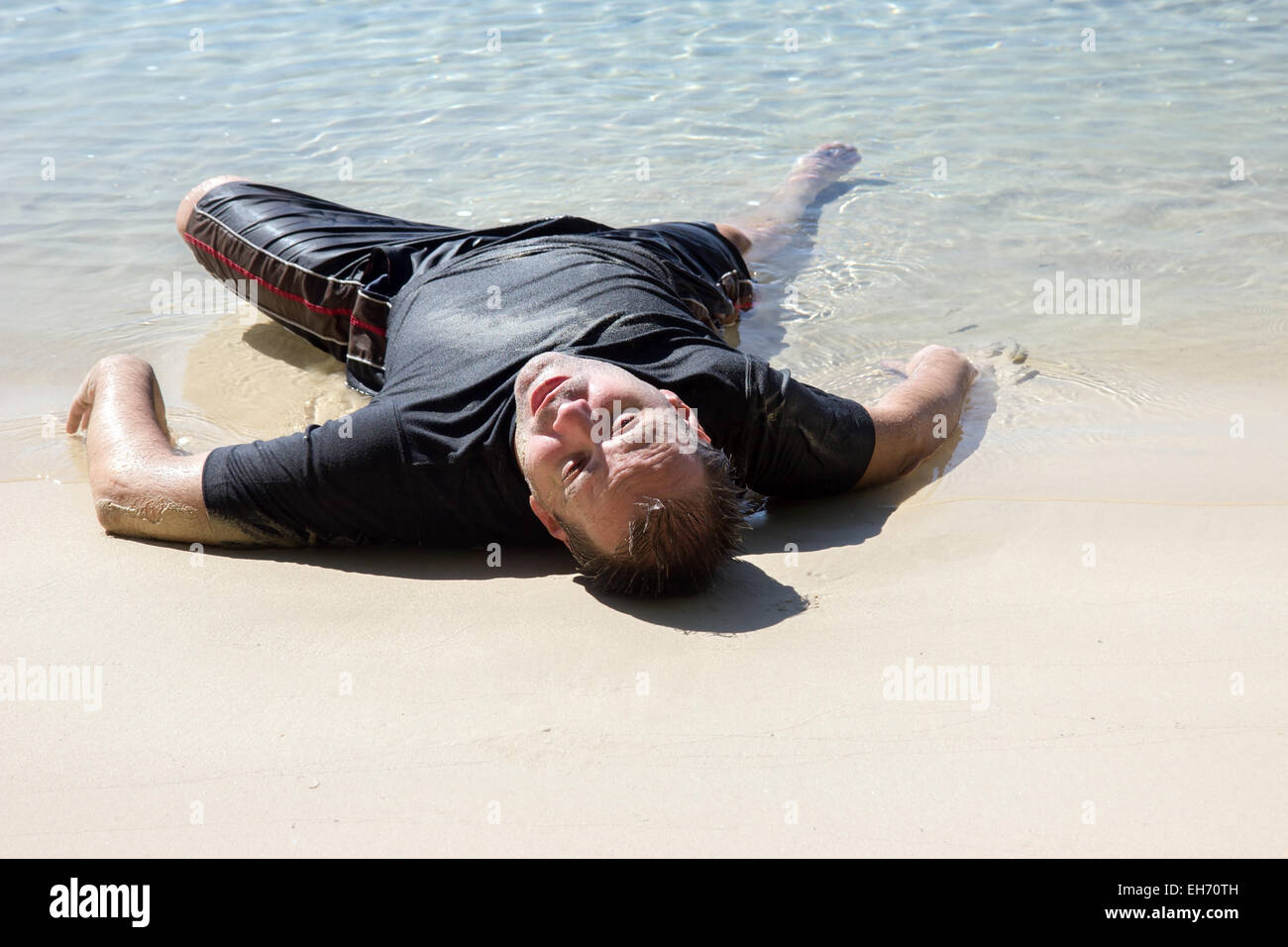 erschöpften Mann kroch aus dem Meer und am Strand liegen Stockfoto