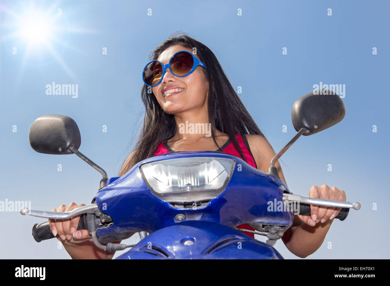Vorderansicht einer Frau sitzt auf einem Roller auf blauem Hintergrund Stockfoto