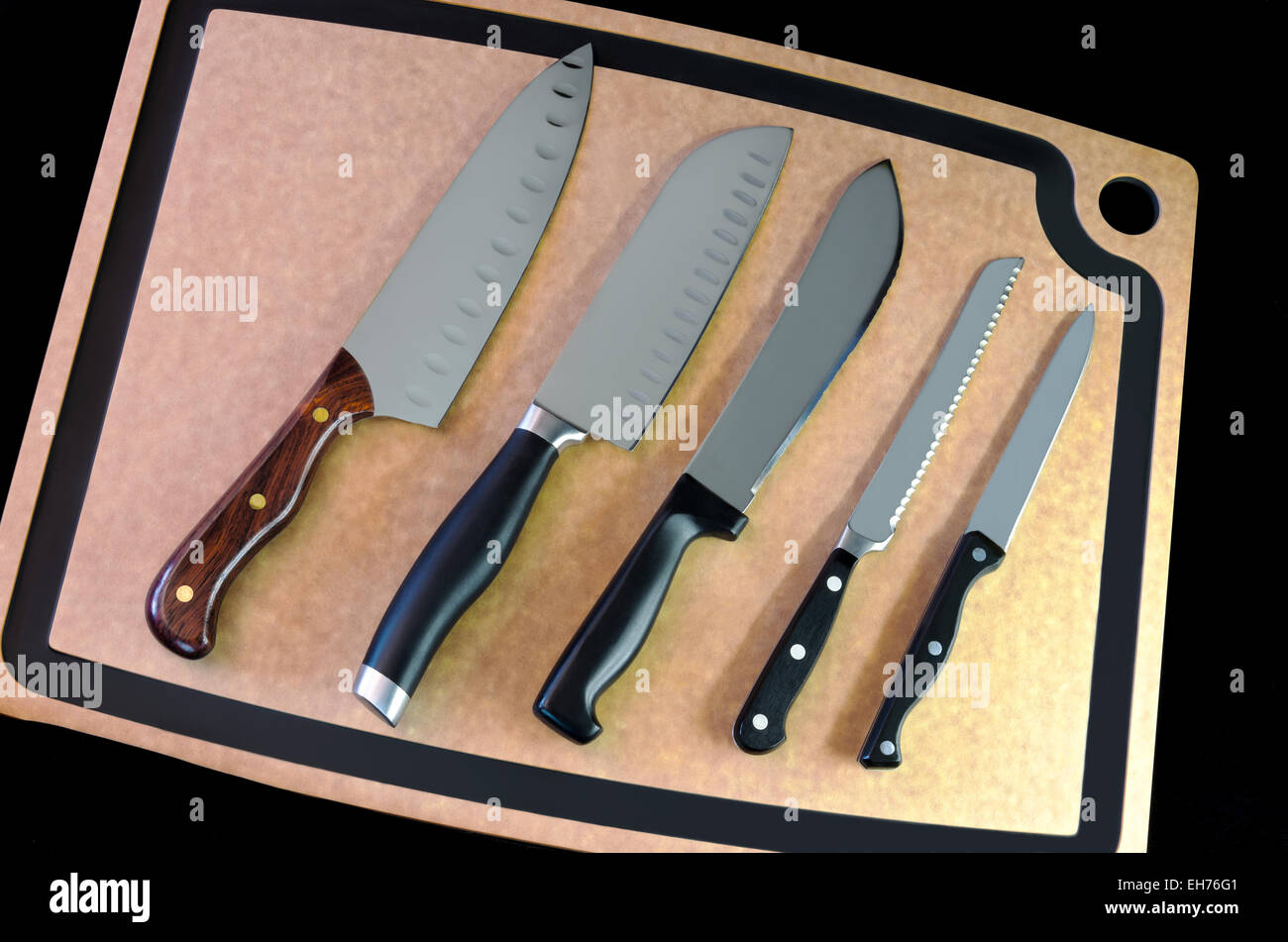 Fünf Messer aus Edelstahl auf Schneidebrett auf schwarzem Hintergrund Stockfoto