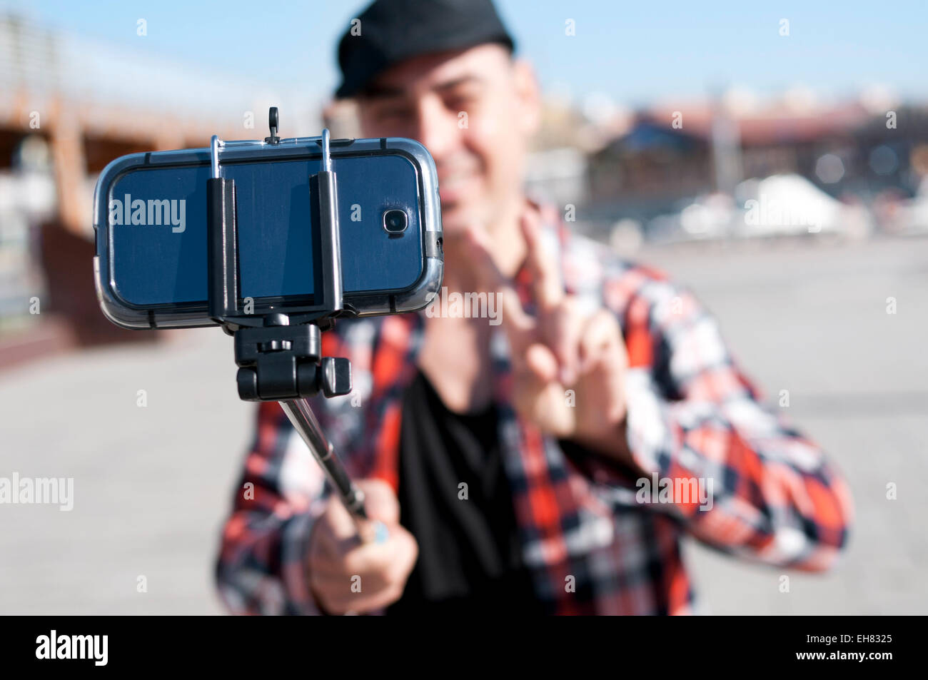 ein junger Mann nimmt ein Selbstporträt mit einem Selfie stick während gibt ein V-Zeichen Stockfoto