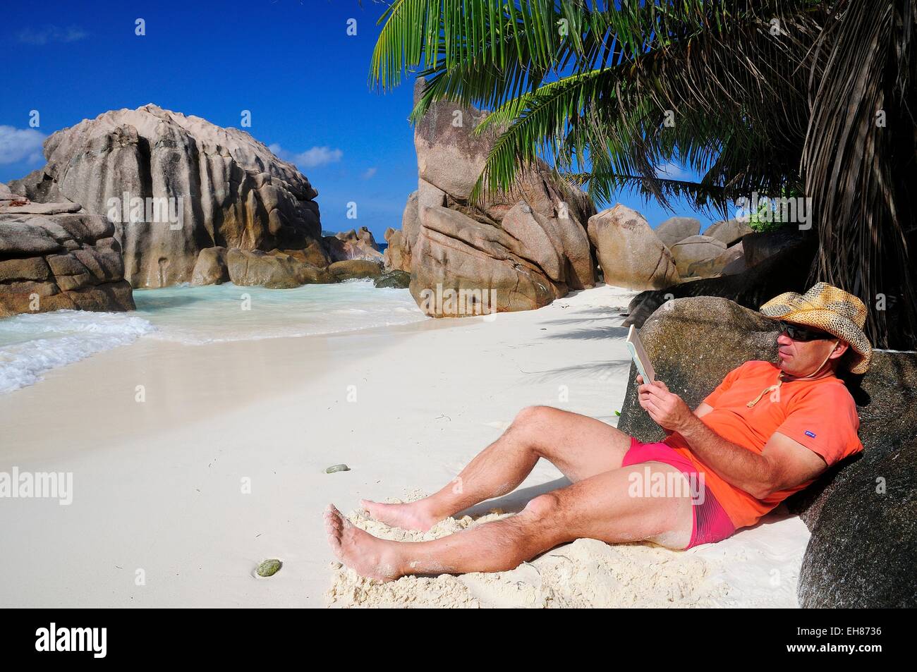 Tourist trägt einen Hut und Buch am Strand von Anse Patates, La Digue Island, La Digue und Inner Islands, Seychellen Stockfoto