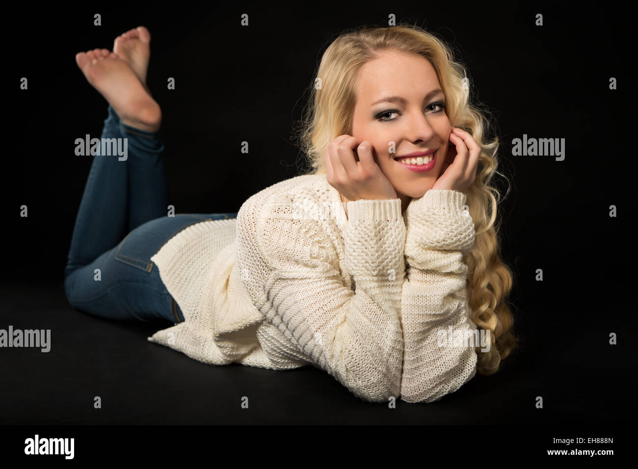 Lächelnde junge Frau liegend auf dem Bauch, Kopf in ihre Hände Stockfoto