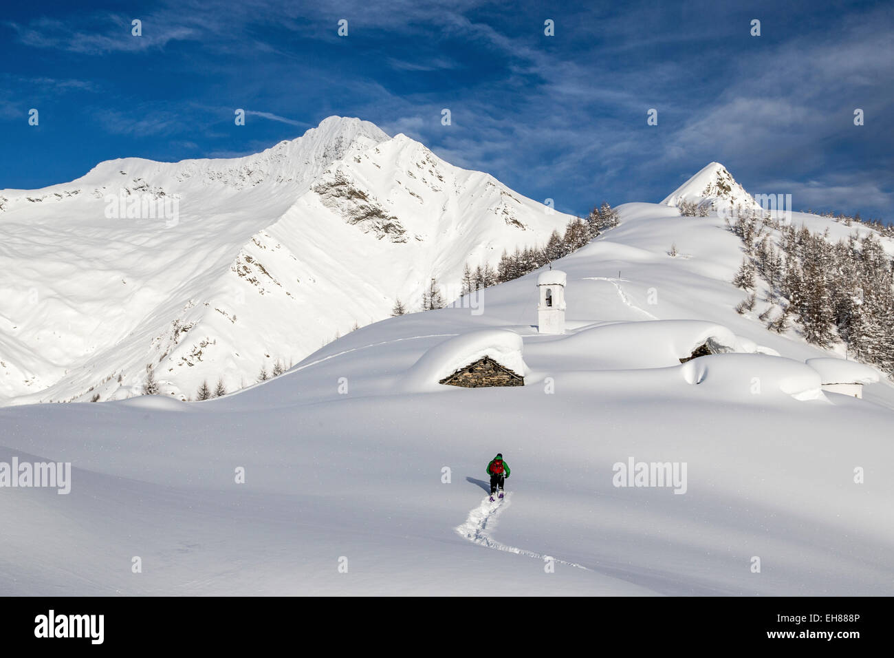 Ein Wanderer, der versucht, das kleine Dorf auf der Alm Scima Ansatz bedeckt in Schnee, Valchiavenna, Lombardei, Italien, Europa Stockfoto