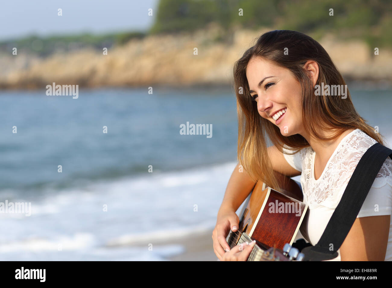 Schöne Gitarrist Frau spielt Gitarre am Strand mit dem Meer im Hintergrund Stockfoto