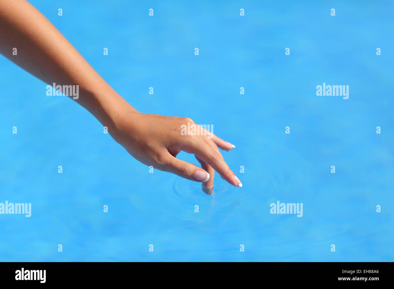 Schöne Frau Hand berühren Wasser in einem Pool mit einem blauen Hintergrund Stockfoto