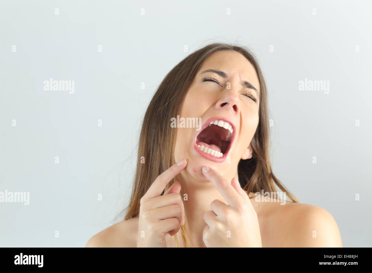 Mädchen weint beim Drücken eines Pickel am Kinn mit einem grauen Hintergrund Stockfoto