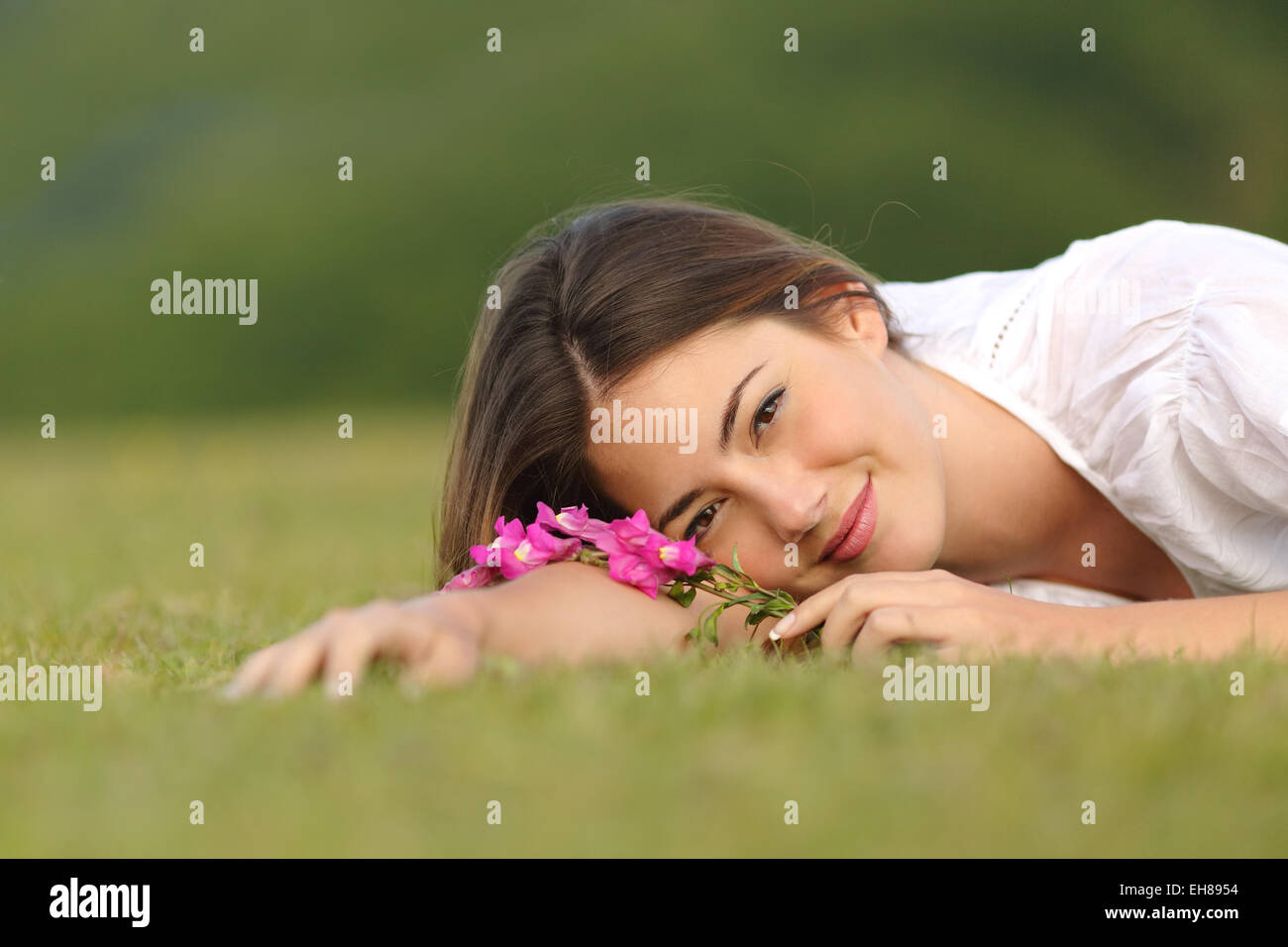 Entspannte Frau ruht auf dem grünen Rasen mit Blumen in einem Park mit einem grünen Hintergrund Stockfoto