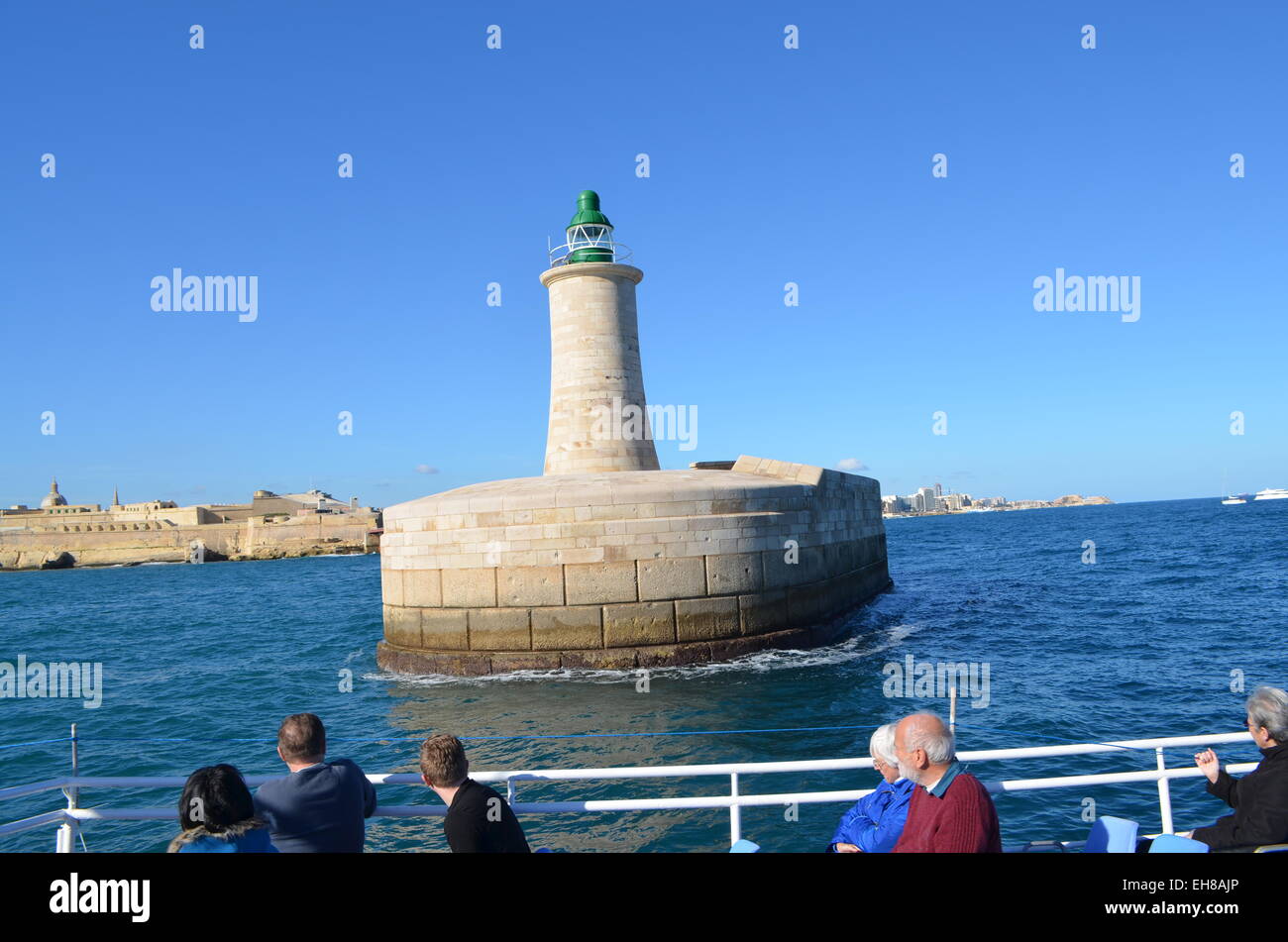Malta, Valletta. Vom Meer in den Grand Harbour hinter dem Hafen gehen Wände und ein Leuchtturm ein Boatful von Touristen. Stockfoto