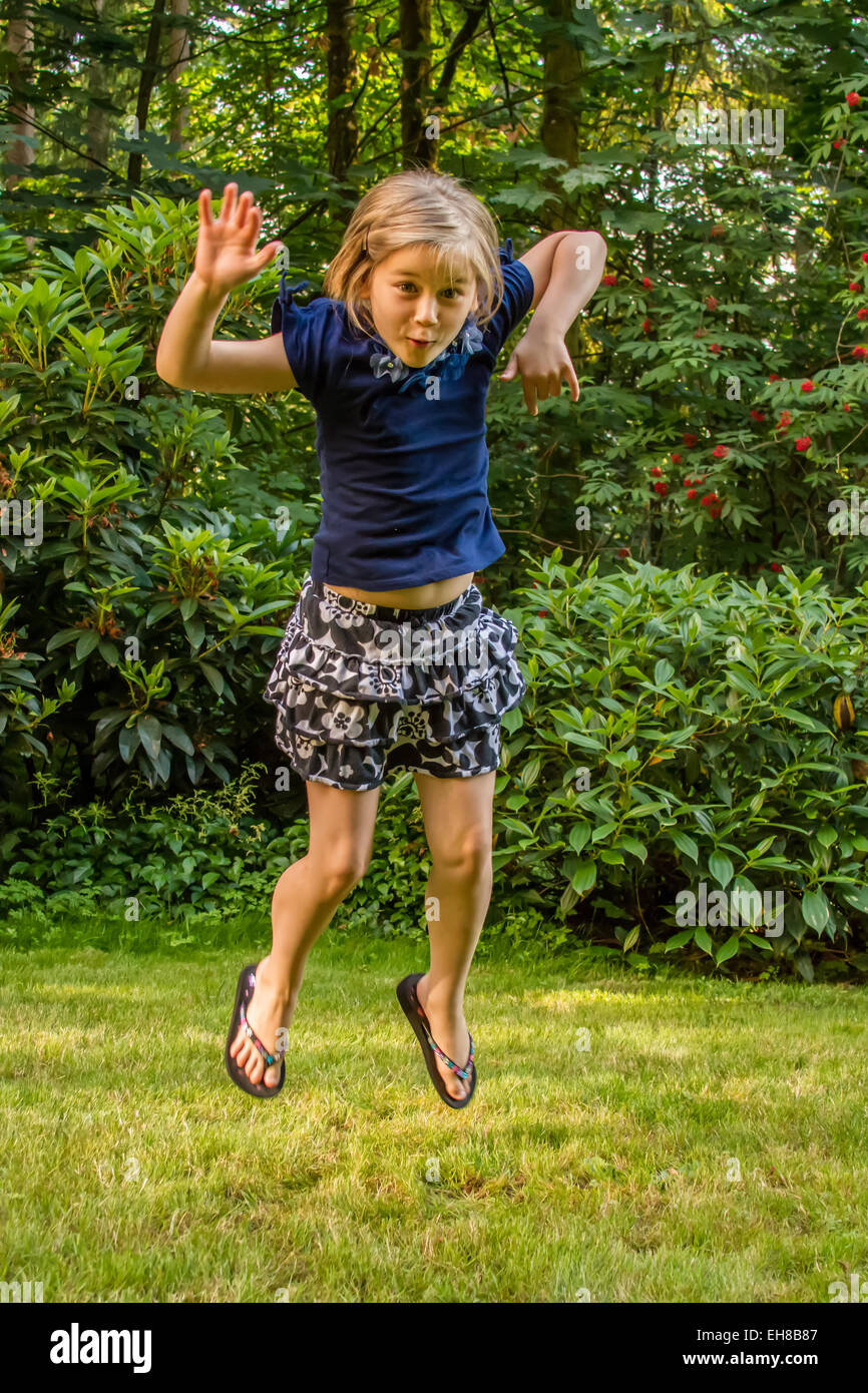 Siebenjähriges Mädchen Angeberei und springen vor Freude in einem Hof in Issaquah, Washington, USA Stockfoto