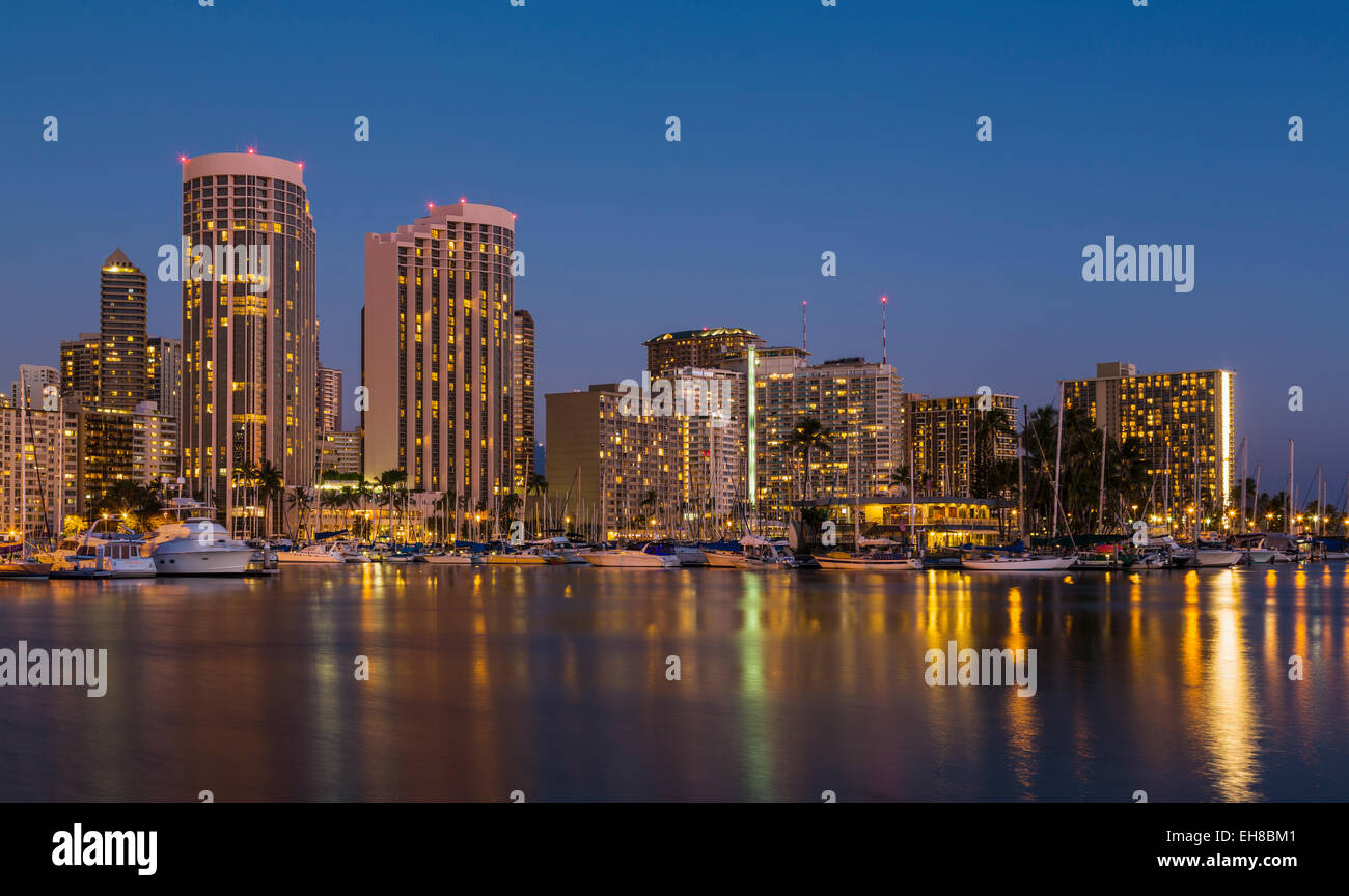 Skyline von Waikiki Bezirk, Honolulu, Hawaii in der Nacht / Dämmerung mit Booten im Hafen Ala Moana und Hilton Hawaiian Village Stockfoto