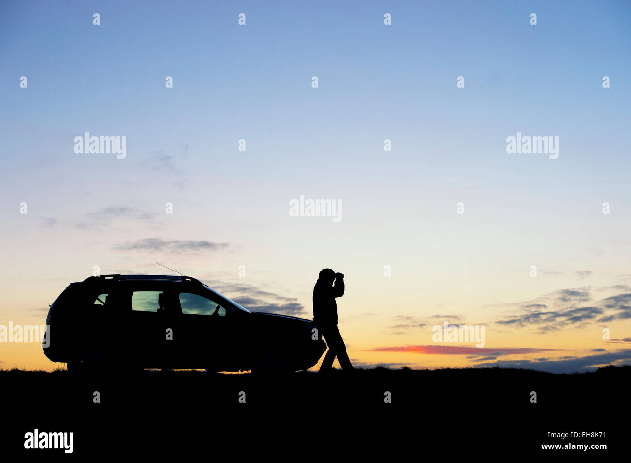 Silhouette-Mann sucht Fernglas neben einem SUV-Auto bei Sonnenaufgang. UK Stockfoto