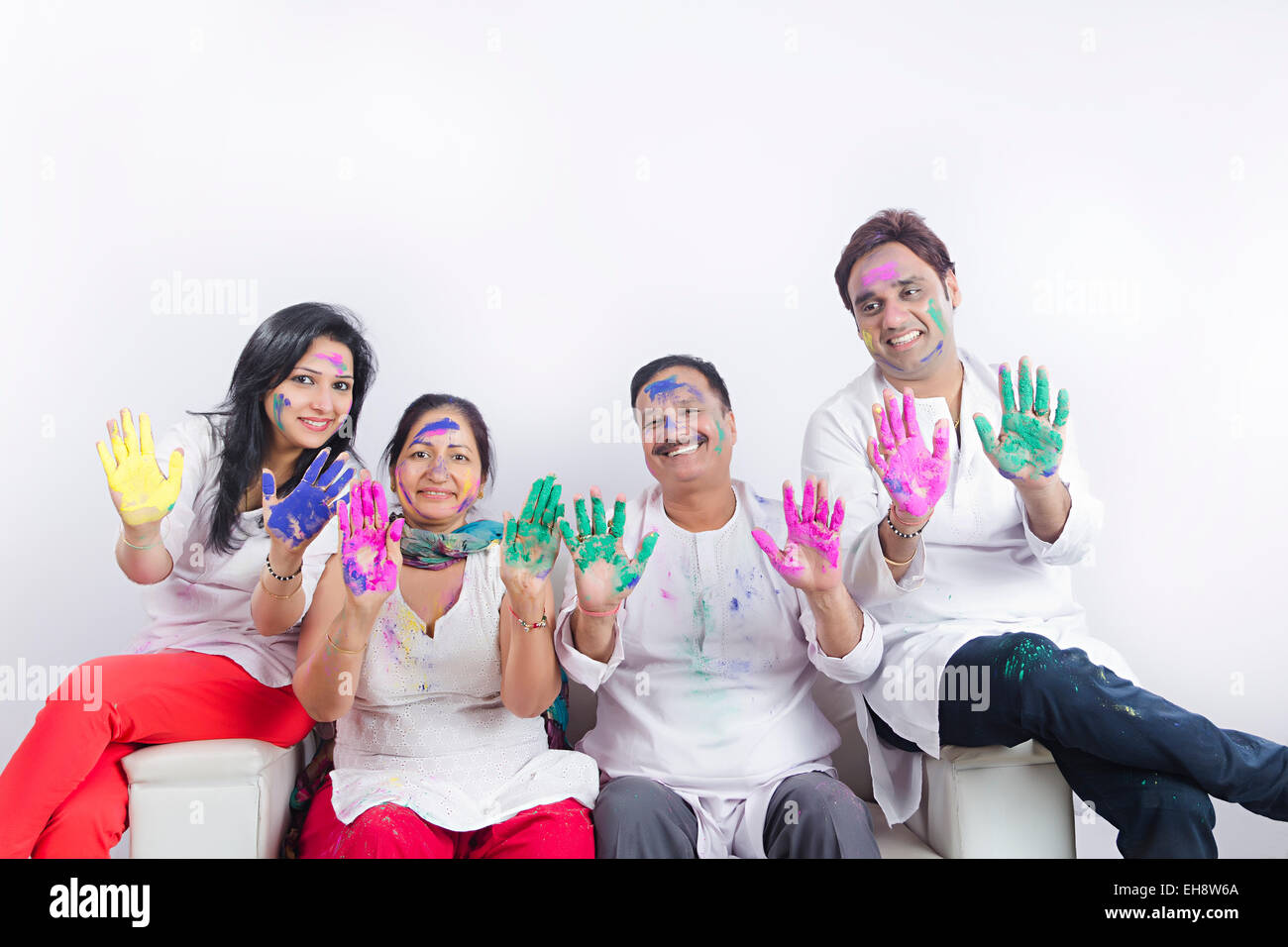 4 indische Erwachsene Eltern Sohn und Schwiegertochter Holi Festival sitzen Sofa hand zeigen Stockfoto