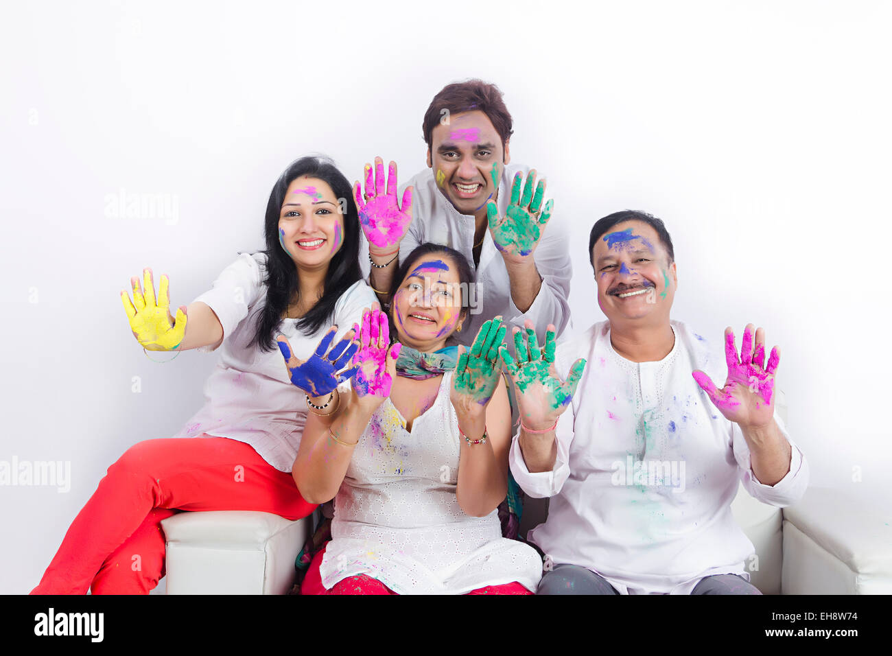 4 indische Erwachsene Eltern Sohn und Schwiegertochter Holi Festival sitzen Sofa hand zeigen Stockfoto