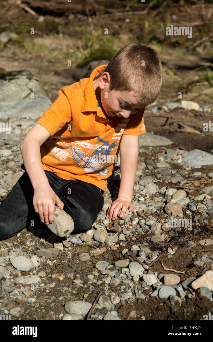 Sieben Jahre alter Junge auf der Suche nach Insekten durch Drehen über Felsen, im Olallie State Park, North Bend, Washington, USA Stockfoto