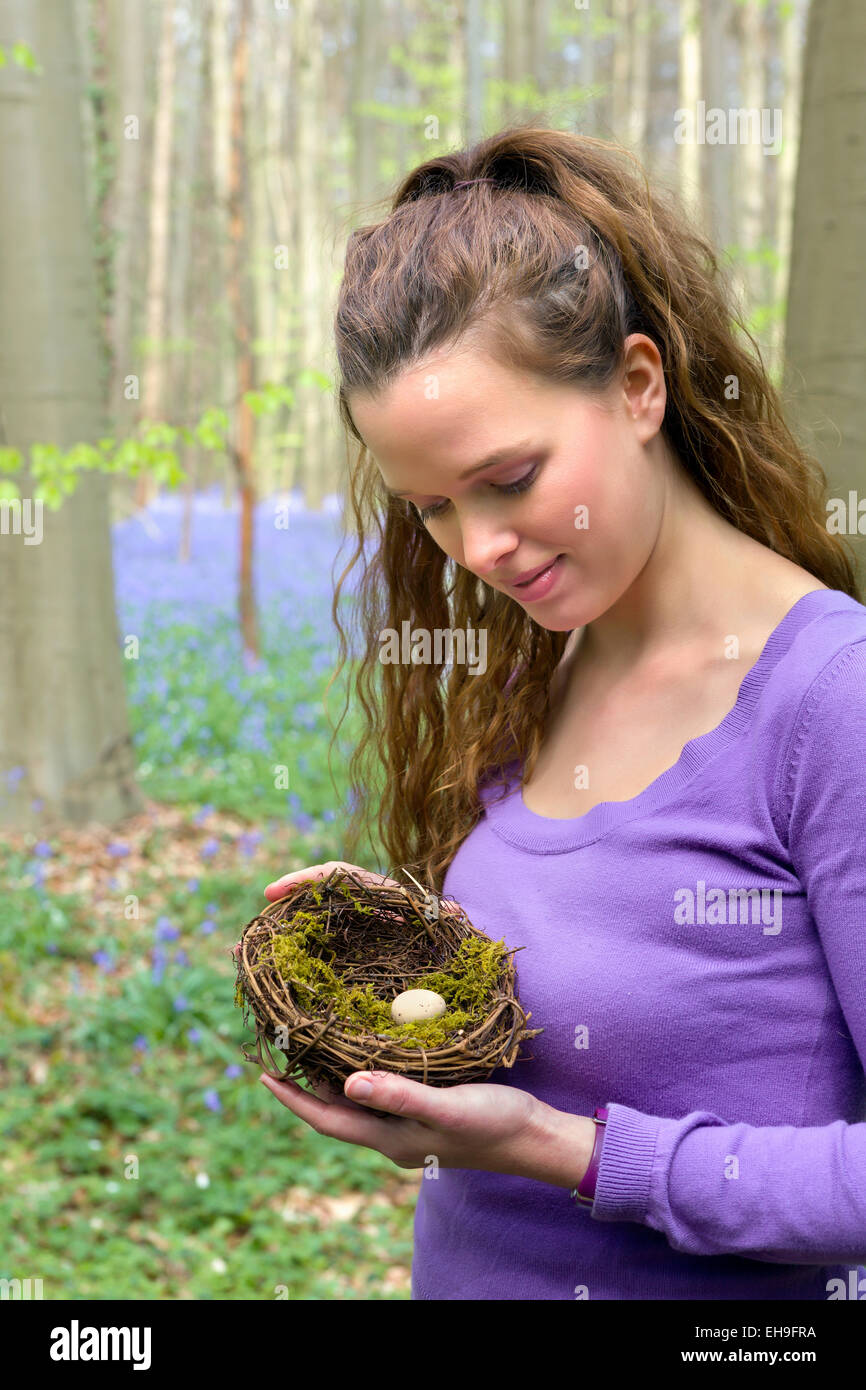 Hübsche junge Frau hält ein Vogelnest in einem Glockenblumen Frühling Wald Stockfoto