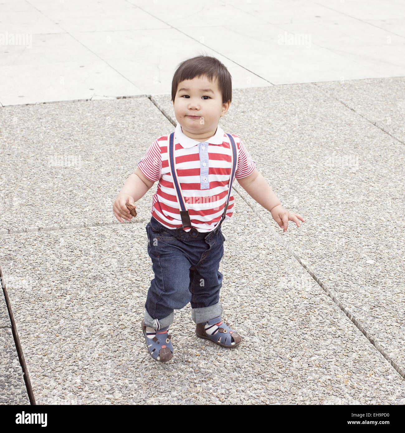 Baby Boy zu Fuß auf den Bürgersteig mit Snack in der hand Stockfoto