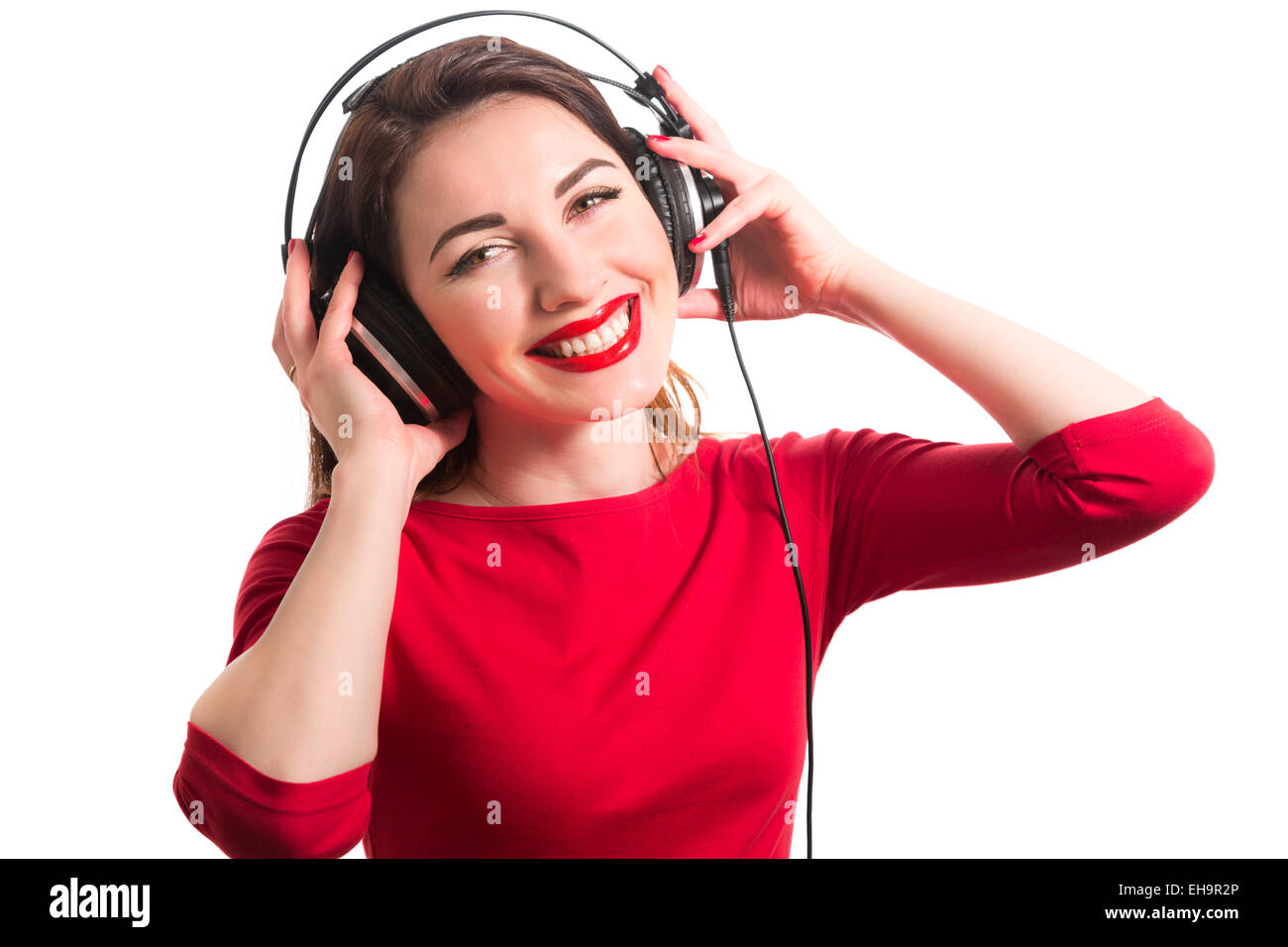 Mädchen Langarm T-shirt tragen rote Lippenstift berühren große Kopfhörern Musik hören lächelnd und Blick auf Kamera isolat Stockfoto