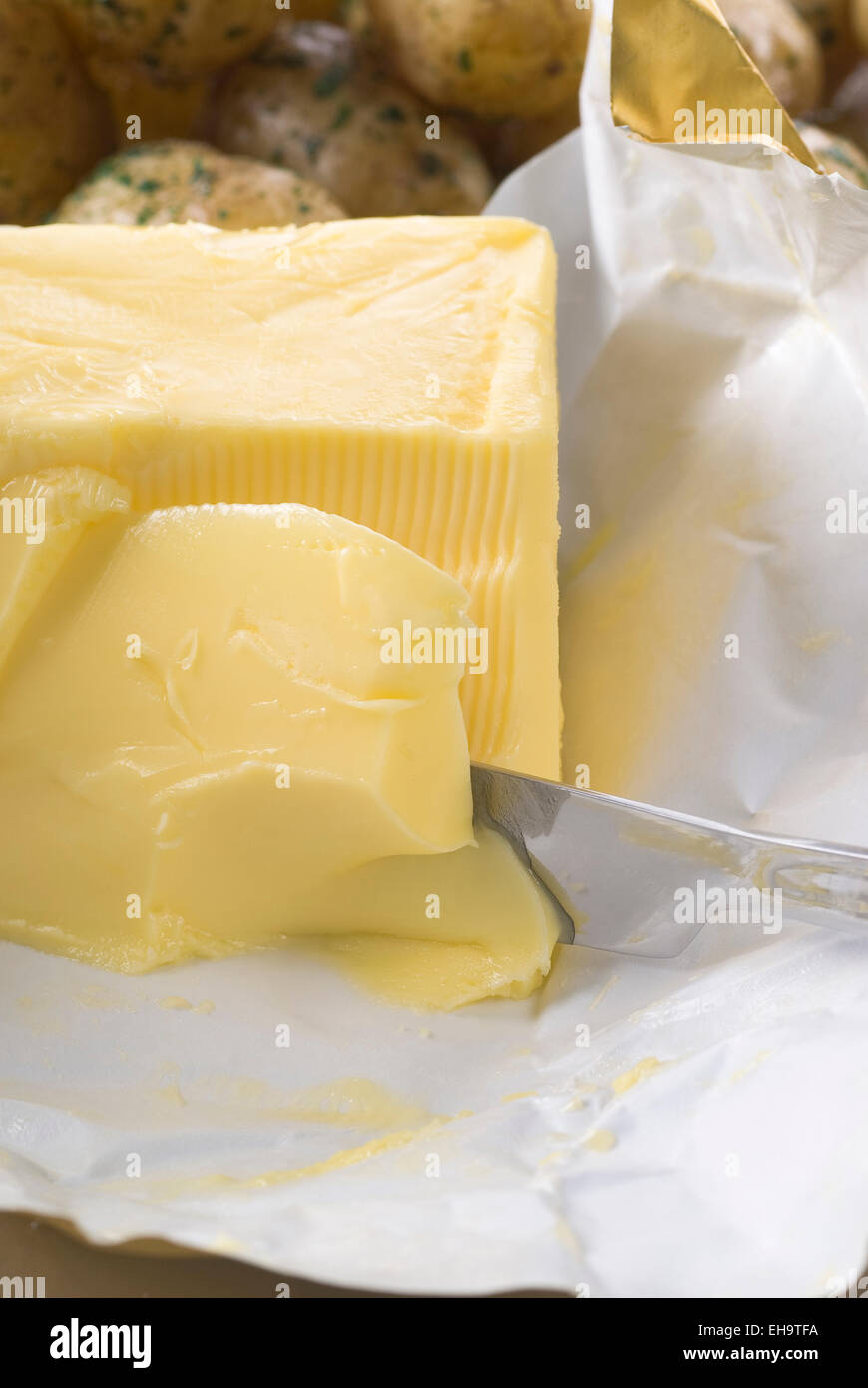 Butter auf dem Papier mit einem Messer. Neue Kartoffeln im Hintergrund. Stockfoto