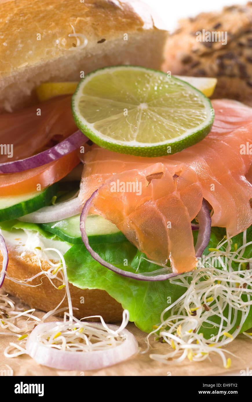 Brot mit Frischkäse, Salat, Gurke, Räucherlachs, Zwiebel, Tomaten, Limette und Zitrone. Stockfoto