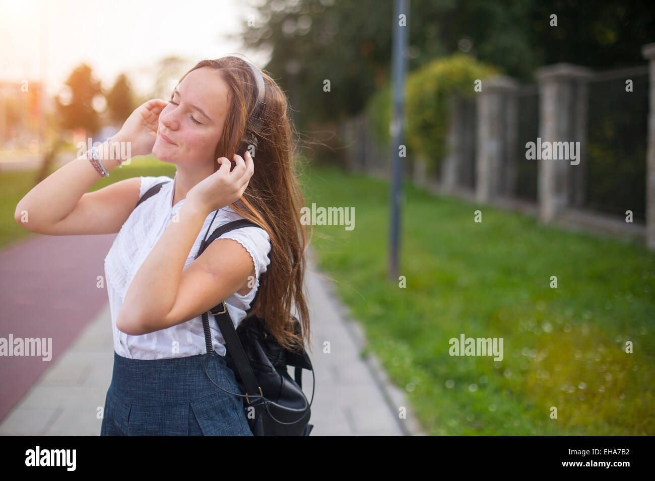 Junge süße Mädchen Musik mit Kopfhörern im Freien in der milden Sonne genießen. Stockfoto