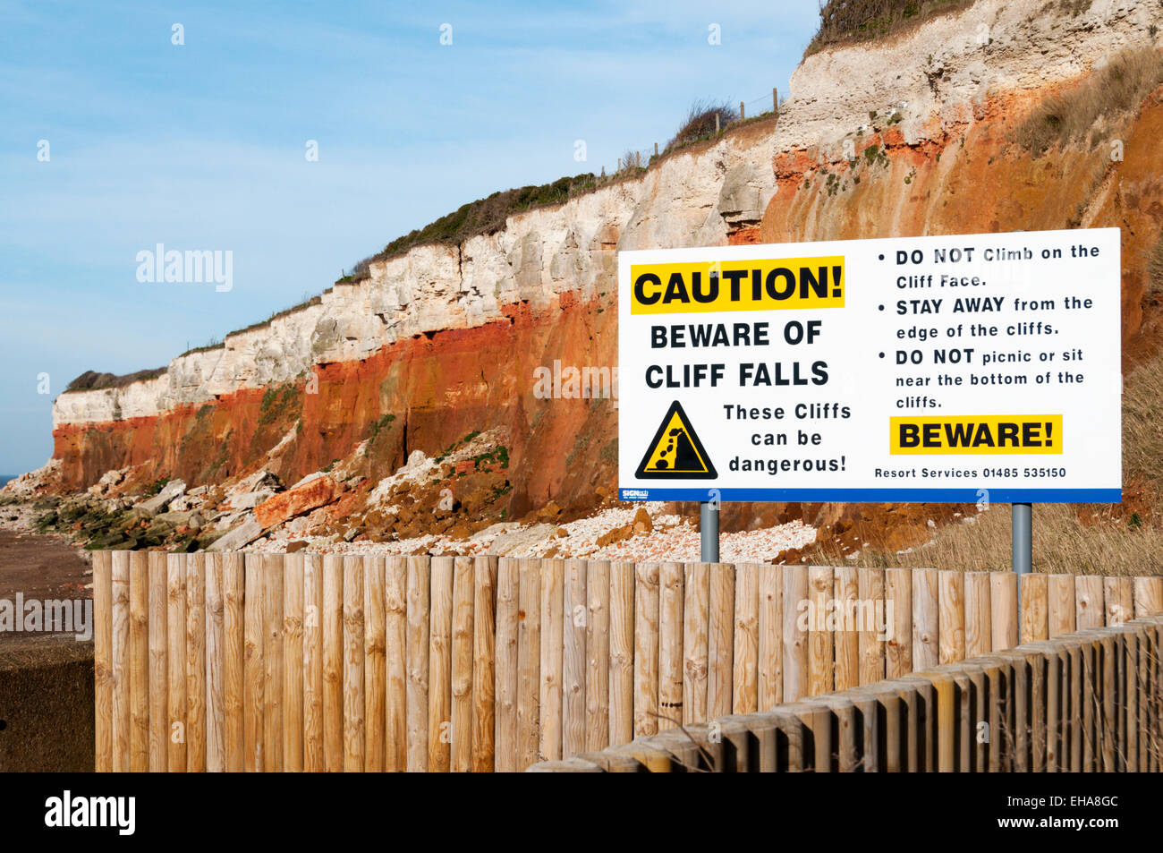 Eine Schild Warnung Klippe fällt vor den roten-weißen gebänderten Klippen von Hunstanton an der Küste von Norfolk, England. Stockfoto