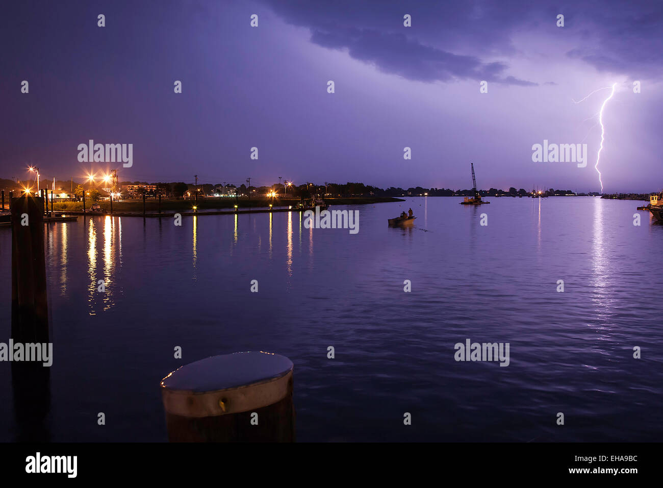 Blitzschlag hinunter auf den Hafen mit einem lila Himmel und ein Boot im Wasser. Stockfoto