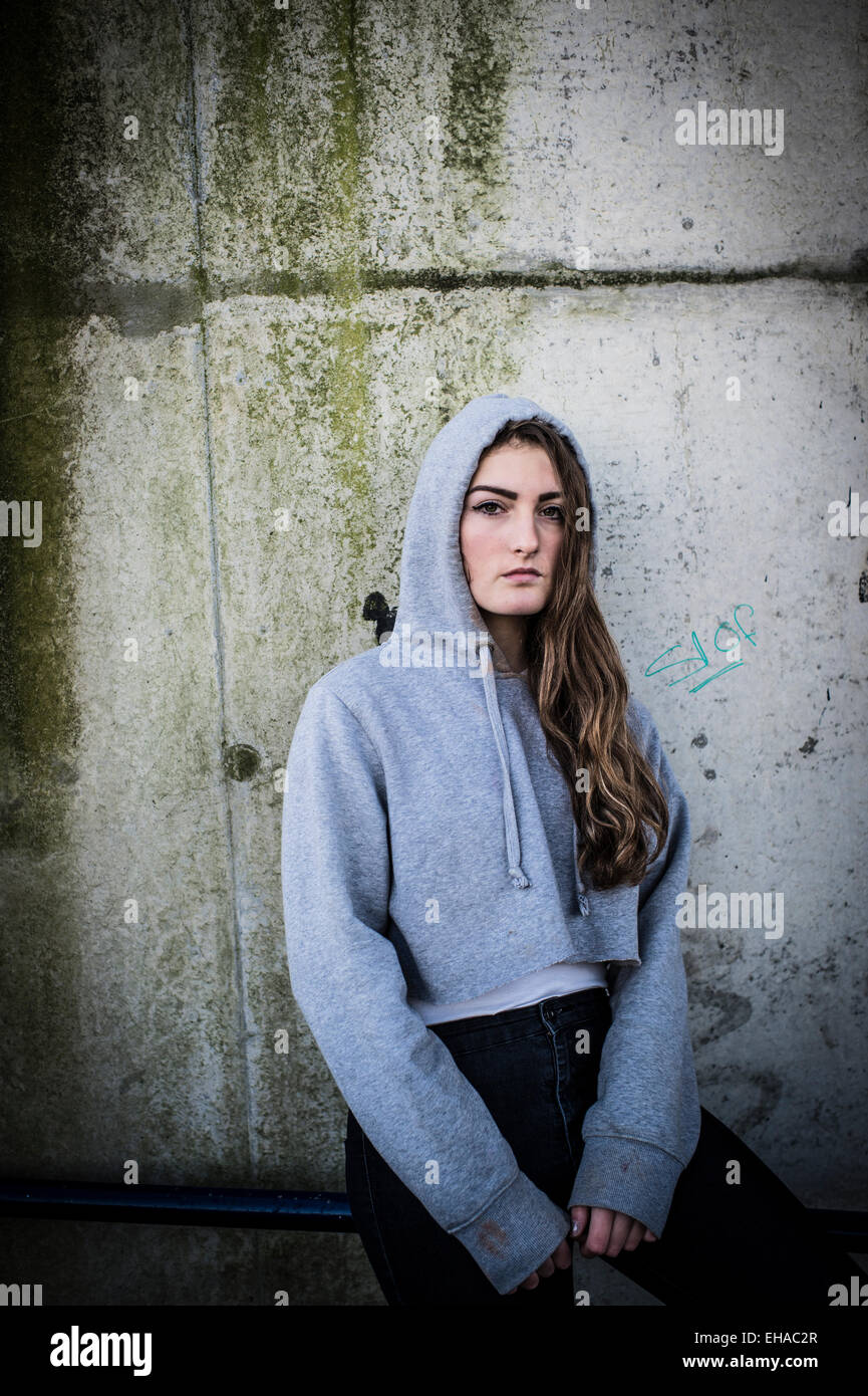 Eine junge 13 14 15 jährige Teenager-Mädchen im freien draußen allein durch  sich selbst trägt eine Greey hoody Hoodie Jacke vor einer schmutzigen  Betonwand UK Stockfotografie - Alamy