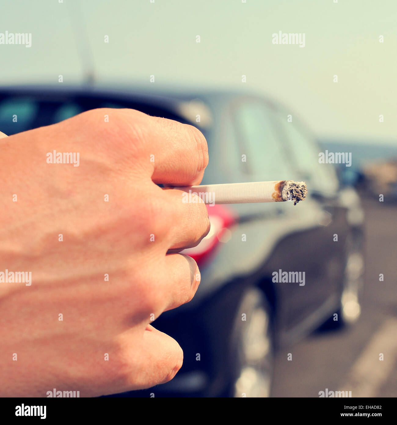 Nahaufnahme eines Mannes mit einer brennenden Zigarette in der Hand und wartet neben einem Auto parkte neben einer nicht befahrenen Straße Stockfoto Nahaufnahme eines Mannes mit einer brennenden Zigarette in der Hand und wartet neben einem Auto parkte neben einer nicht befahrenen Straße Stockfoto