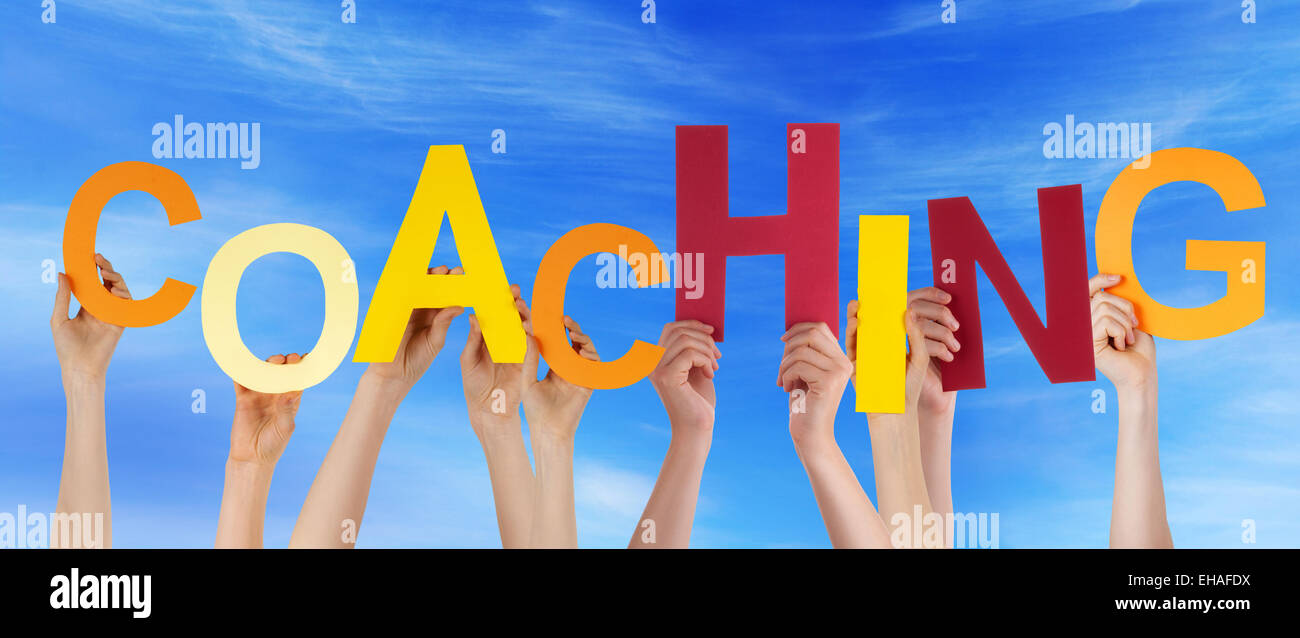Viele Hände halten bunte Buchstaben oder Zeichen Gebäude das englische Wort Coaching auf blauen Himmel und kaukasische Menschen Stockfoto