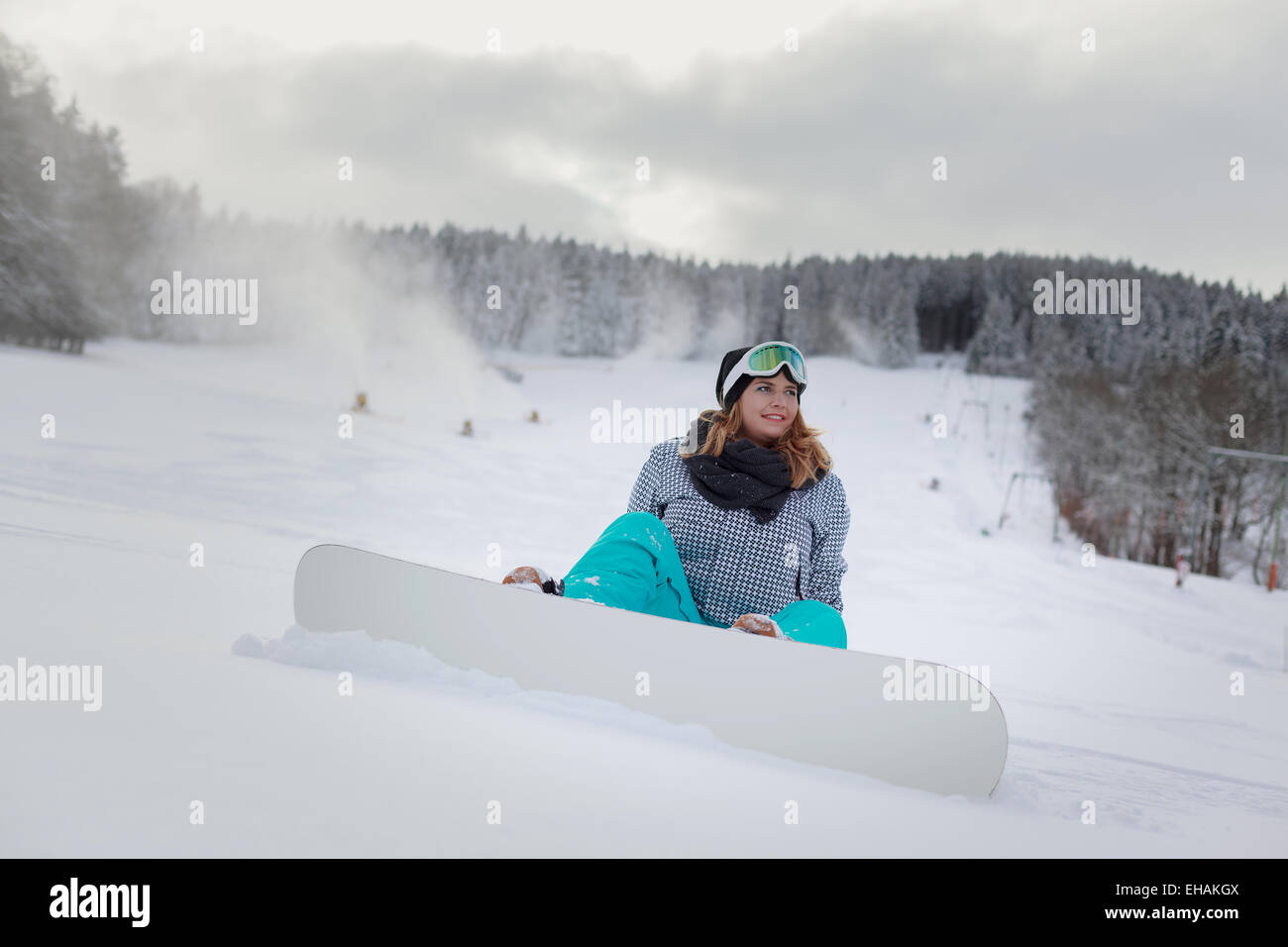 Junge Frau sitzt mit Snowboard im Schnee auf dem Berg Stockfoto