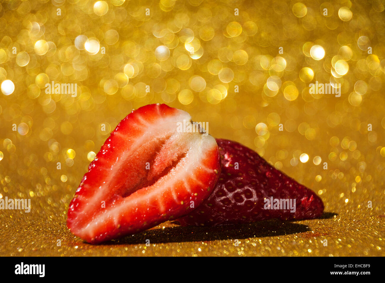 Zwei Scheiben einer Erdbeere auf Goldgrund glitzernden Withbokeh. Stockfoto