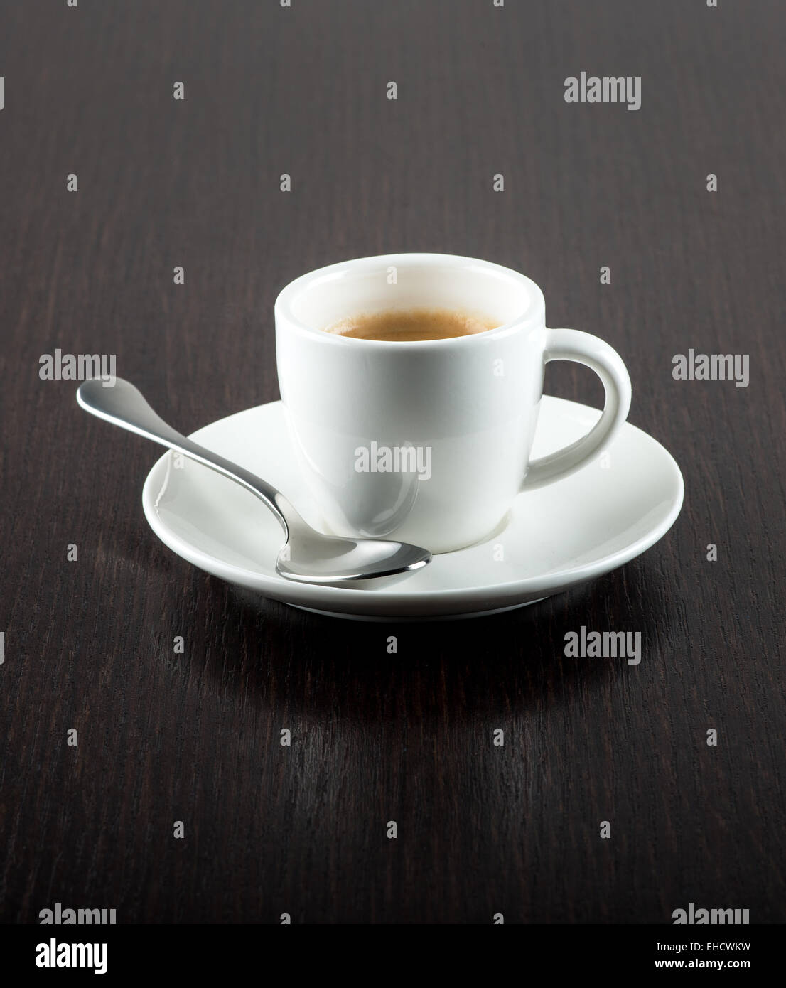 Nahaufnahme von Kaffee in weiße Tasse auf Untertasse mit silbernen Löffel auf dunkle Holzmaserung Tisch Stockfoto