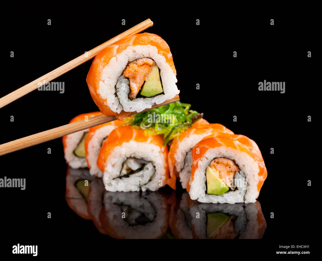 Köstliche Sushi-Rollen mit Stäbchen auf schwarzen Tisch serviert. Stockfoto