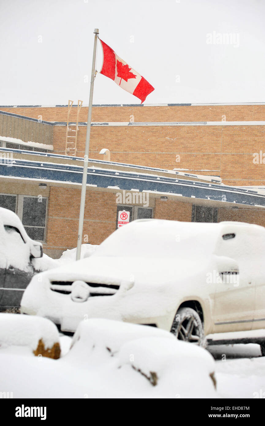 Eine kanadische Flagge weht der Wind über verschneite Autos auf einem Parkplatz in London, Ontario. Stockfoto