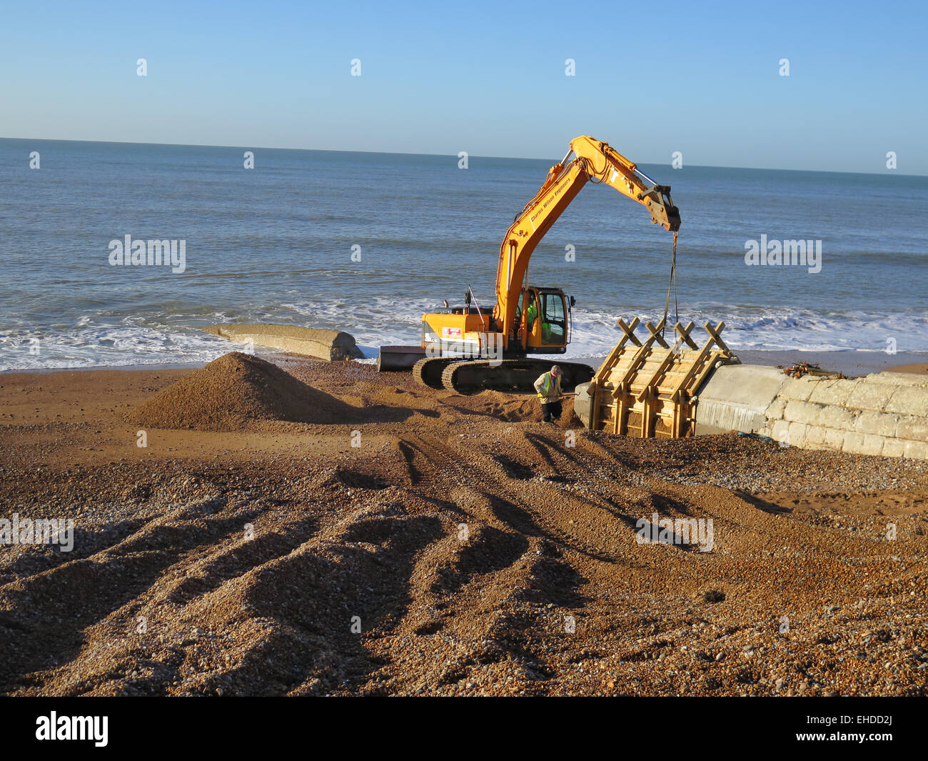 Ein Caterpillar Bagger mit Thorne Tiefbau Arbeiter hölzerne Formen von neuem Beton zu entfernen vorbereitet Buhnen gebaut am Strand von Hove, East Sussex. Stockfoto