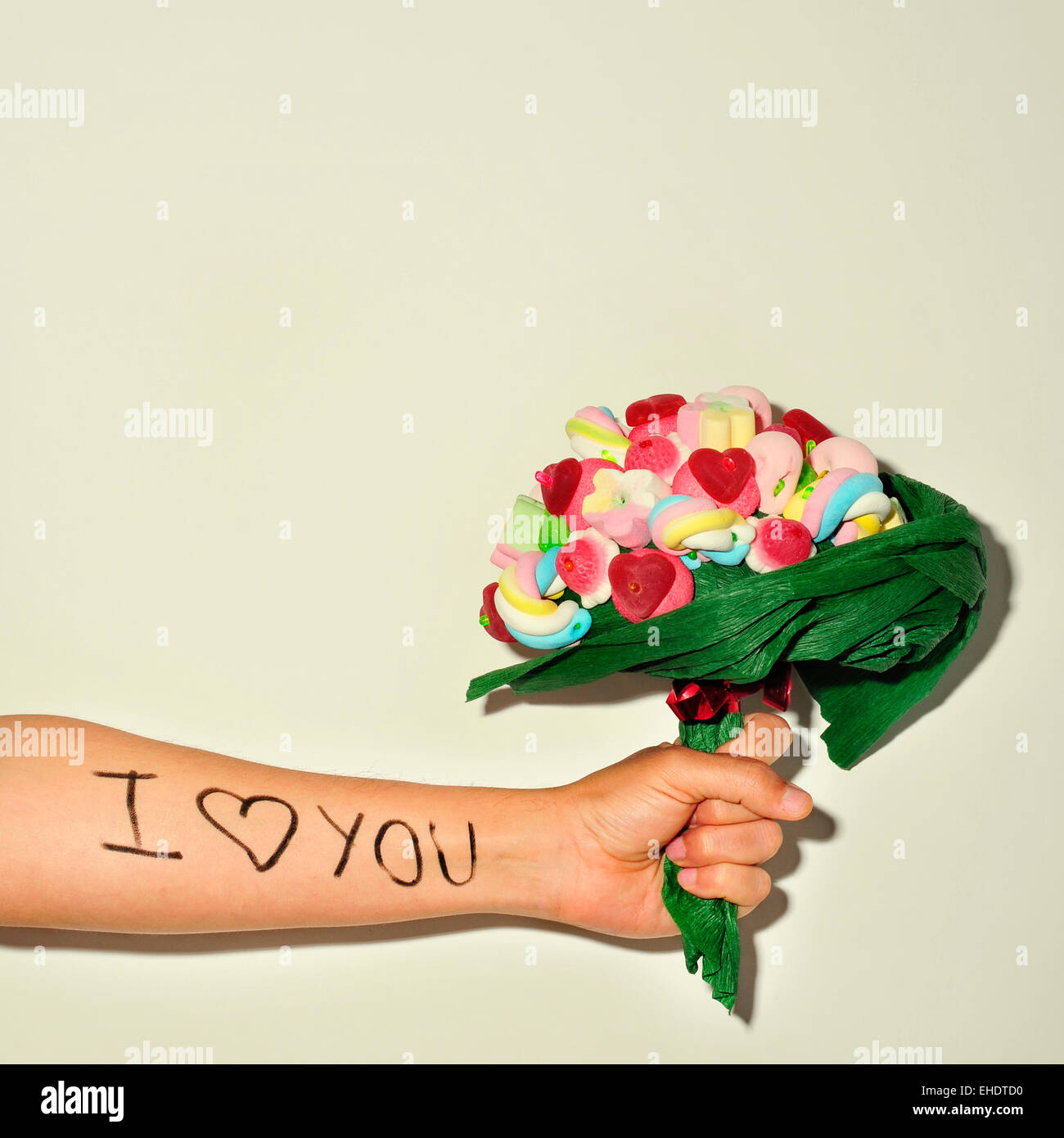 ein junger Mann mit einem Candy Bouquet und den Satz Liebe ich dich geschrieben in seinem Unterarm Stockfoto