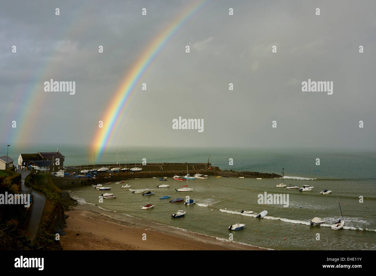 Hafen von Wales New Quay. Doppelter Regenbogen über Wellenbrecher.  Boote bei Liegeplätze in der geschützten Bucht. Stockfoto