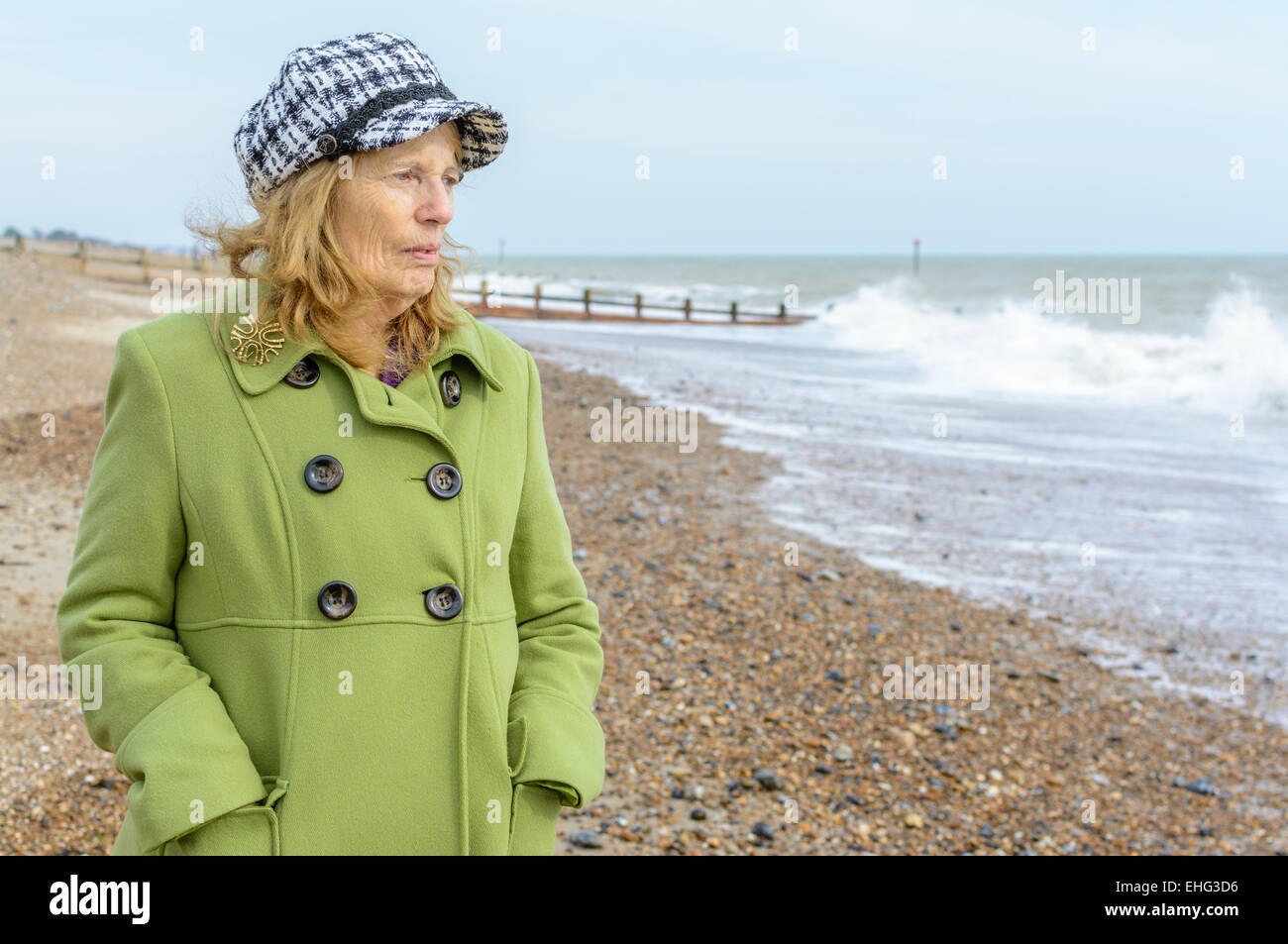 Ältere Frau gekleidet herzlich in der Kälte am Strand, Blick auf das Meer. Stockfoto