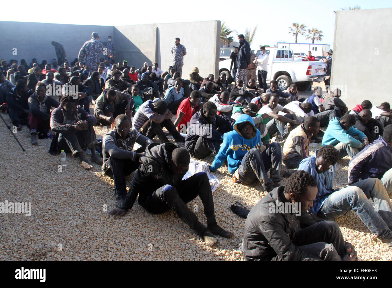 (150313)--Tripolis, März 13, 2015(Xinhua)--illegale Einwanderer sitzen in einem Hof, bewacht von der libyschen Polizei in Tripolis, Libyen, am 13. März 2015. Libyen ist seit langem ein Durchgangsort für Migranten, die darauf abzielen, Malta, Italien und anderswo in Europa zu erreichen. (Xinhua/Hamza-Türkei) Stockfoto
