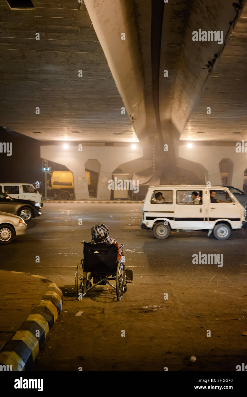 Ein Alter Mann im Rollstuhl durch eine stark befahrene Straße von Nizamuddin, Neu-Delhi betteln. Stockfoto