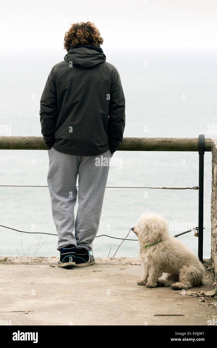 SANTANDER, Spanien - 11. März 2015: ein junger Mann und sein Hund blicken auf das Meer an einem Wintermorgen Stockfoto