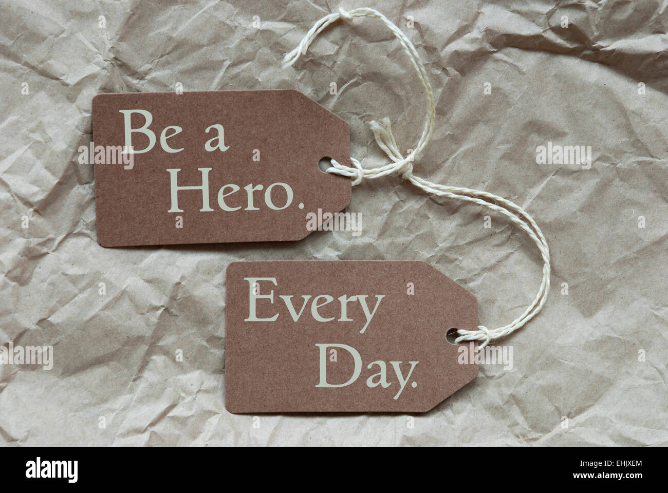 Zwei braune Etiketten oder Tags mit weißen Band auf zerknittertes Papierhintergrund mit englischen Leben Zitat ein Held zu sein, jeden Tag Vintage oder R Stockfoto