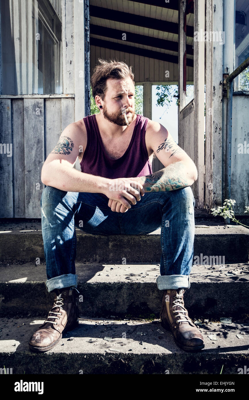Ein junger Mann sitzt außen verlassenes Haus und Zigaretten rauchen. Stockfoto