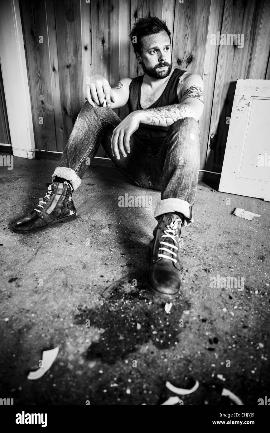 Punk Rocker oder Redneck sitzt auf dem Boden und Rauch in einem unordentlichen Haus. Stockfoto